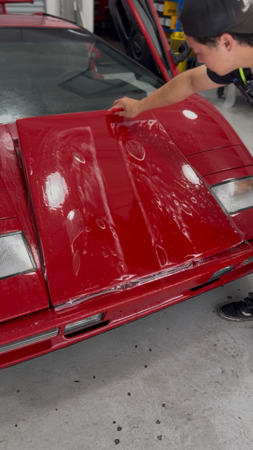 Technician applying paint protection film to a red sports car hood